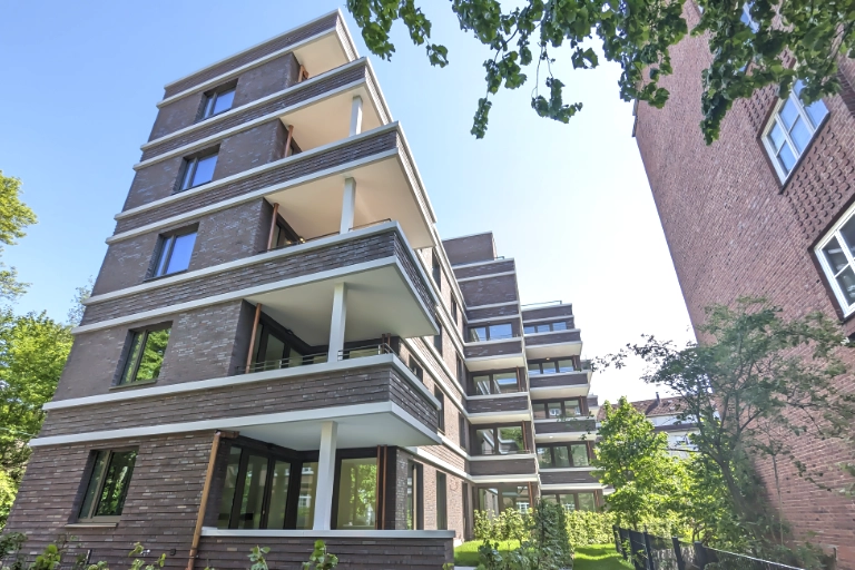 Neubau eines modernen Mehrfamilienhauses in Hamburg mit Klinkerfassade, großzügigen Balkonen und gepflegten Grünflächen. Hochwertige Wohnimmobilie mit zeitgemäßer Architektur und attraktivem Wohnumfeld.